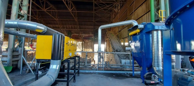 מערכת תעשייתית לסינון אוויר במפעל – מכלים כחולים וצהובים מחוברים בצינורות מתכת, על רקע מבנה תעשייתי פתוח.