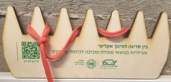 מסרגת עץ עם חוט אדום שזור, ולצידה טקסט 'בין סריגה לחינוך אקלימי – פעילויות בנושאי פסולת וסביבה וקוד QR למידע נוסף