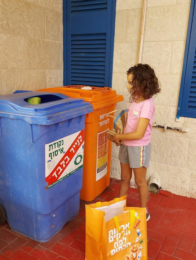 ילדה ממחזרת אריזה בפח הכתום לצד פח כחול למחזור נייר